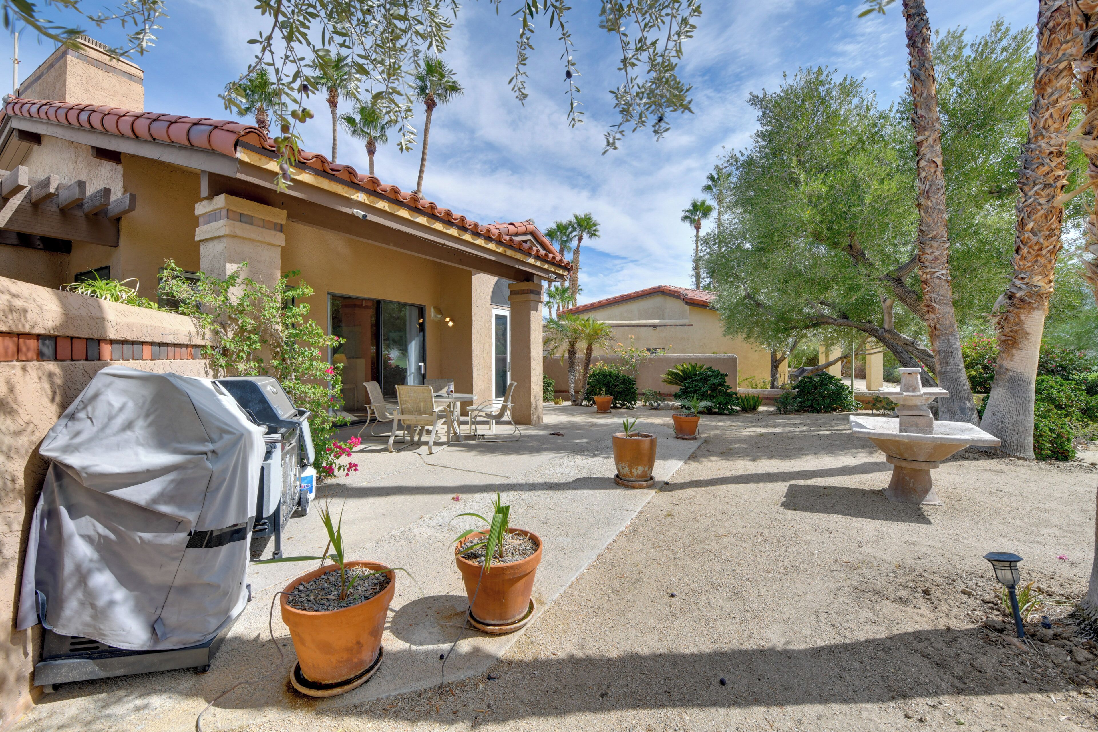 A patio area with a barbecue grill, potted plants, outdoor furniture, and a stone fountain.