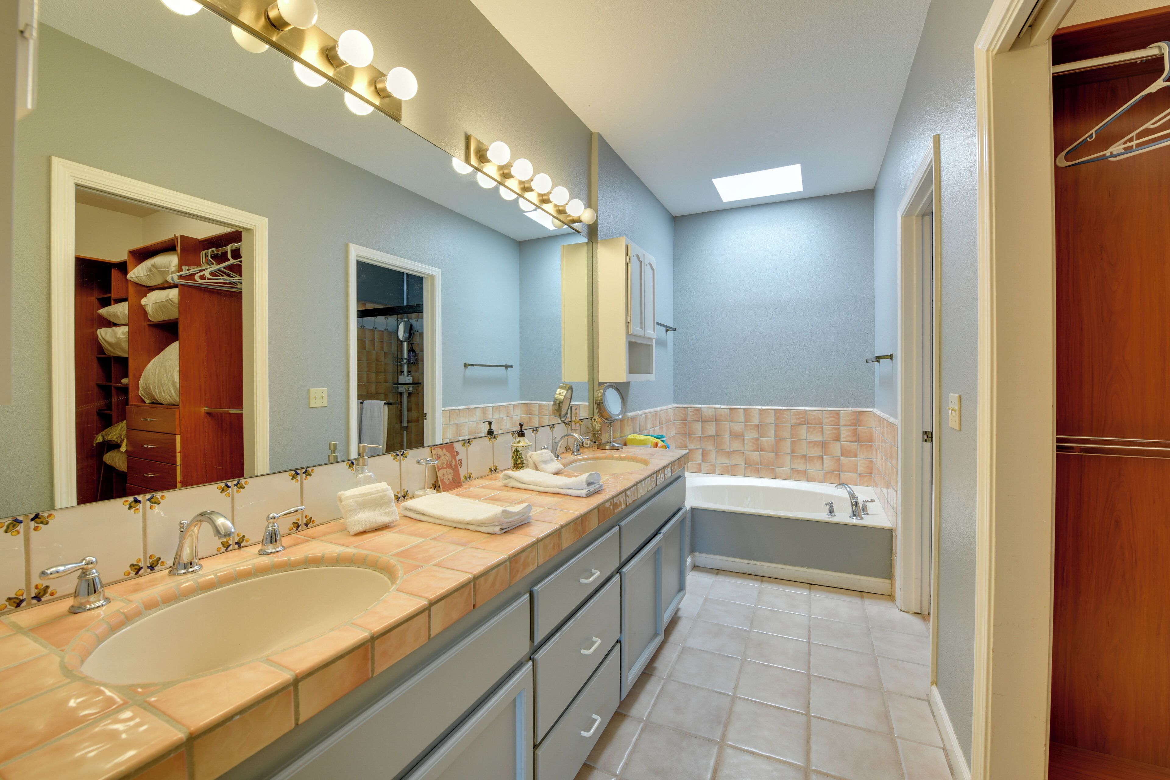 A modern bathroom with a large vanity, a double sink, a bathtub, and a walk-in closet.