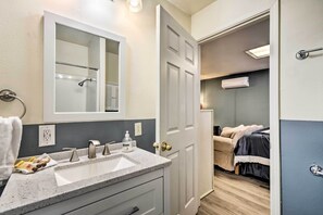 A bathroom with a sink, mirror, and shower. There is a bed visible through an open door in the adjacent room. - California Countryside Retreat: Pets Welcome! (Delhi)