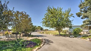 Una calle residencial con pavimento, un jardín con rocas y plantas, y árboles.