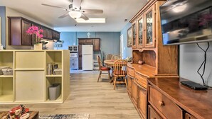Una cocina moderna con armarios de madera, un comedor con mesa y sillas de madera, un ventilador de techo y un televisor de pantalla plana.