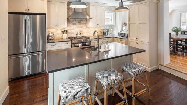 A modern kitchen with a large island, stainless steel appliances, and wooden bar stools.
