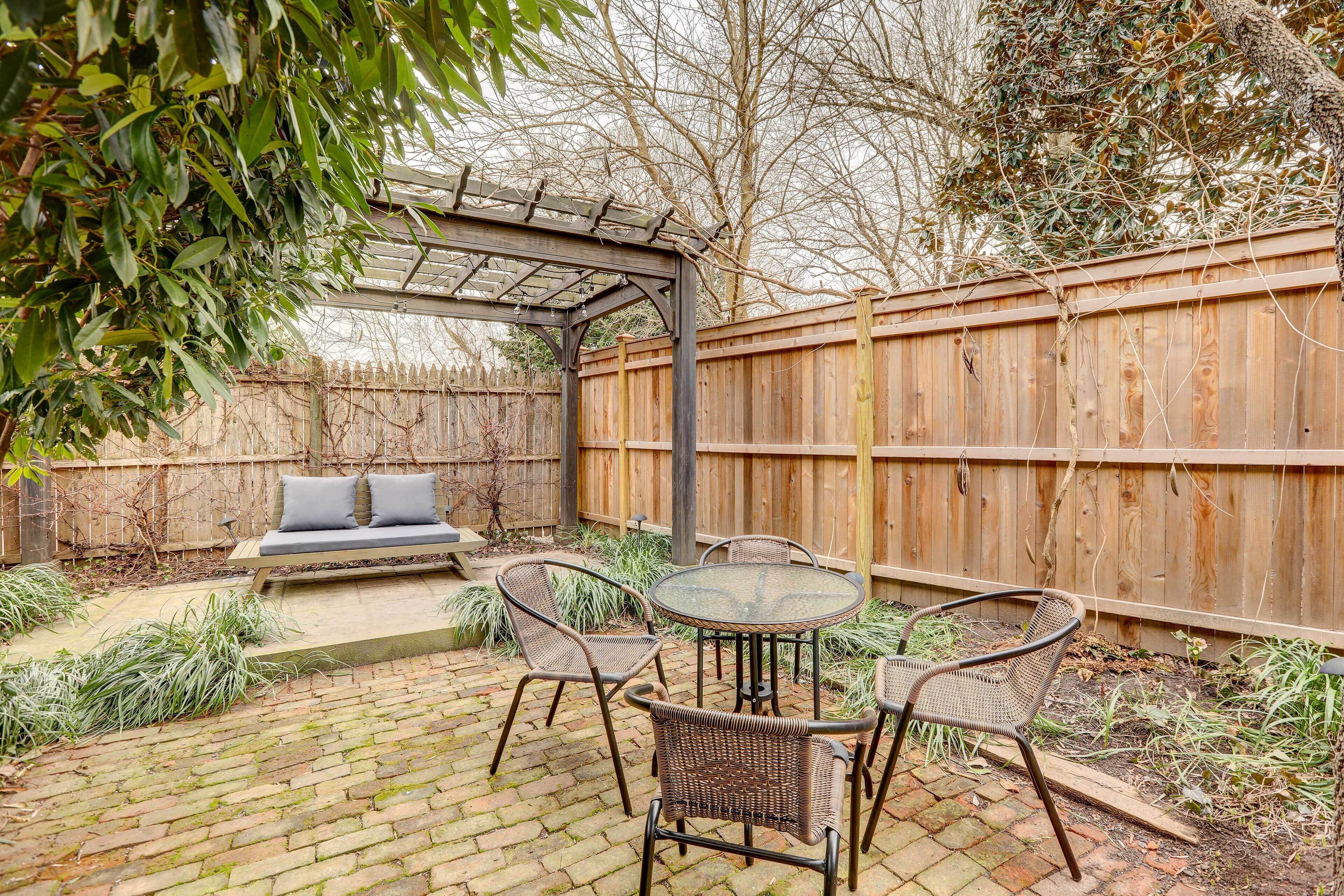 A patio with wicker furniture, a glass table, and a wooden fence.