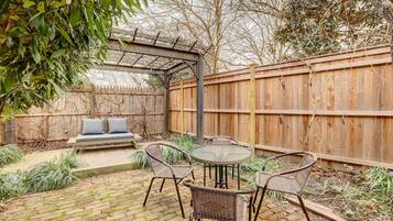 A patio with wicker furniture, a glass table, and a wooden fence.