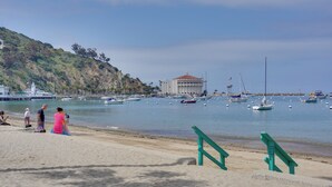 A beach with a large building, boats, and people.