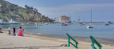 A beach with a large building, boats, and people.