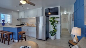 A modern kitchen with white cabinets, a stainless steel refrigerator, a ceiling fan, and a bar area with stools.