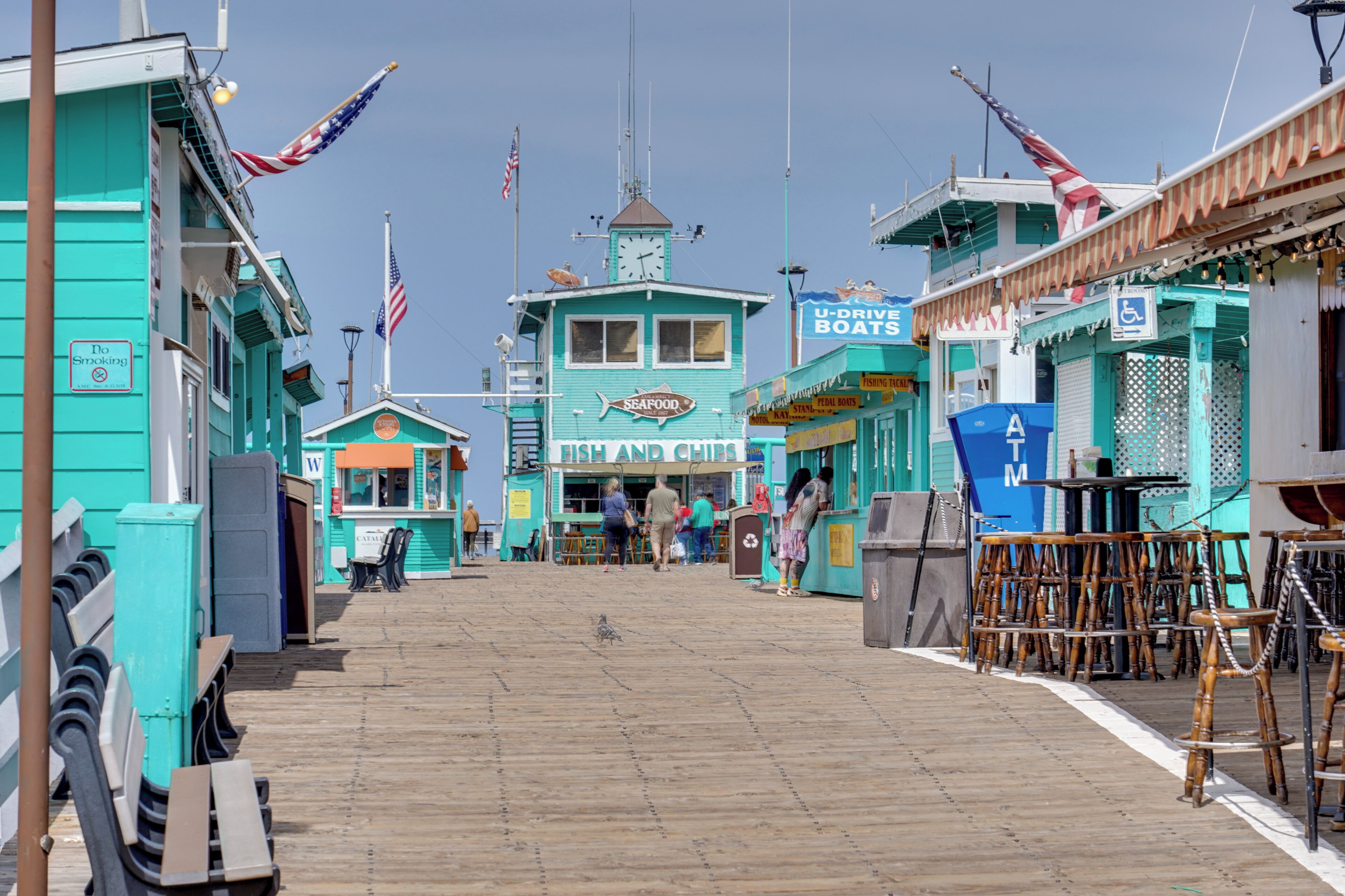 A boardwalk with turquoise buildings, a seafood sign, and a U-Drive Boats sign.