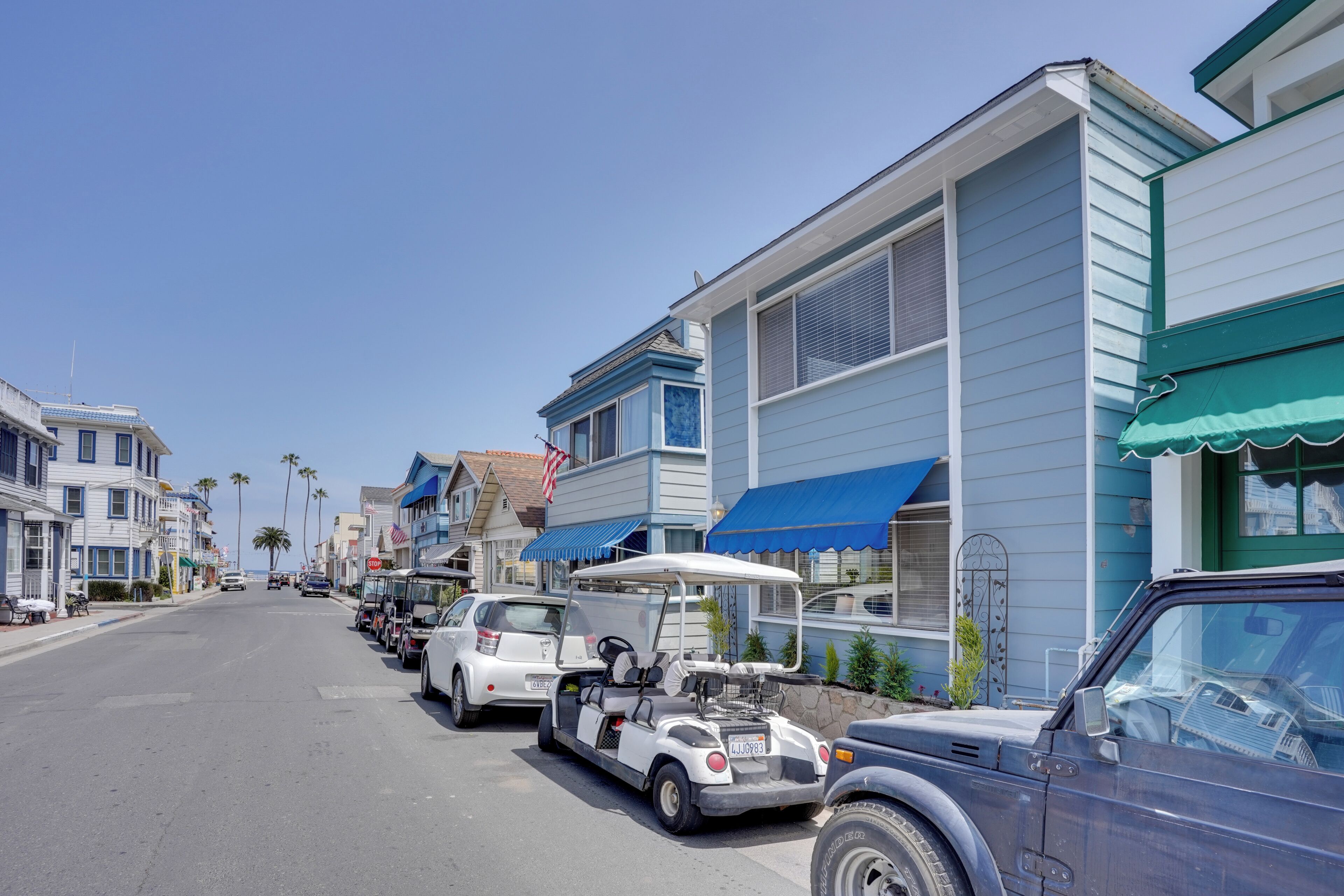 A coastal street lined with blue and white houses, parked cars, and a golf cart.