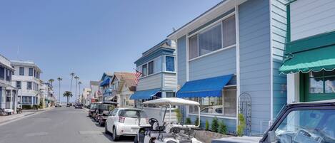 A coastal street lined with blue and white houses, parked cars, and a golf cart.