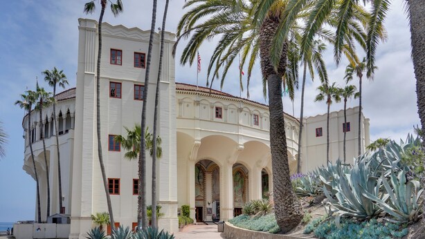 A large, white building with arched windows and a central entrance, surrounded by palm trees and agave plants.