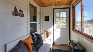 A cozy room with a wooden ceiling, a white couch with cushions, a small table with a decorative item, and a door with a window. - Centrally-located Mountain Getaway in Lead! (Lead)