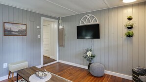 A room with a wooden floor, a white bench, a TV mounted on the wall, and a door leading to another room. - Centrally-located Mountain Getaway in Lead! (Lead)
