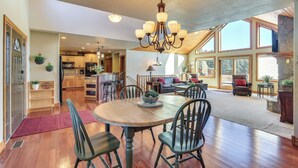 A spacious living area with a wooden dining table, multiple chairs, a chandelier, and a view of the kitchen and dining area through large windows. - Keystone Cabin ~ 9 Mi to Mt Rushmore! (Hermosa)