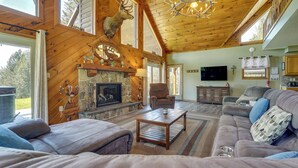 A spacious living room with a fireplace, a mounted deer head, and a large window. - 3-acre Benezette Cabin: Hot Tub, Grill & Mtn View (Benezette)