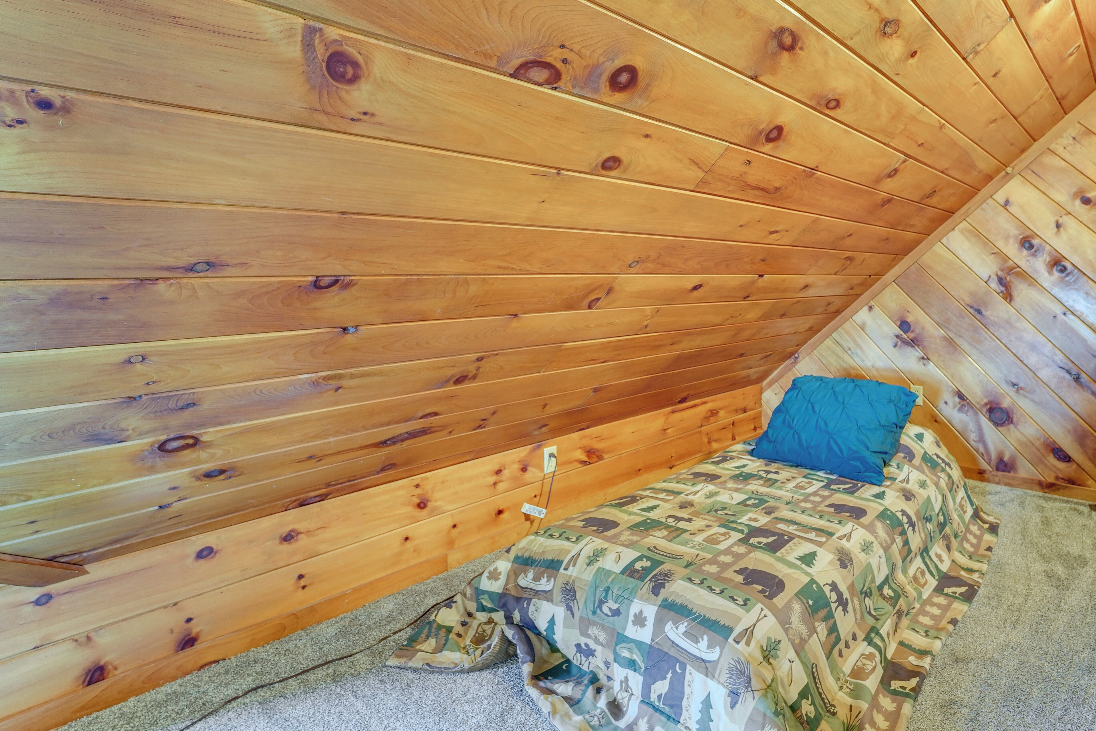 A small, wooden-paneled room with a single bed and a blue pillow.