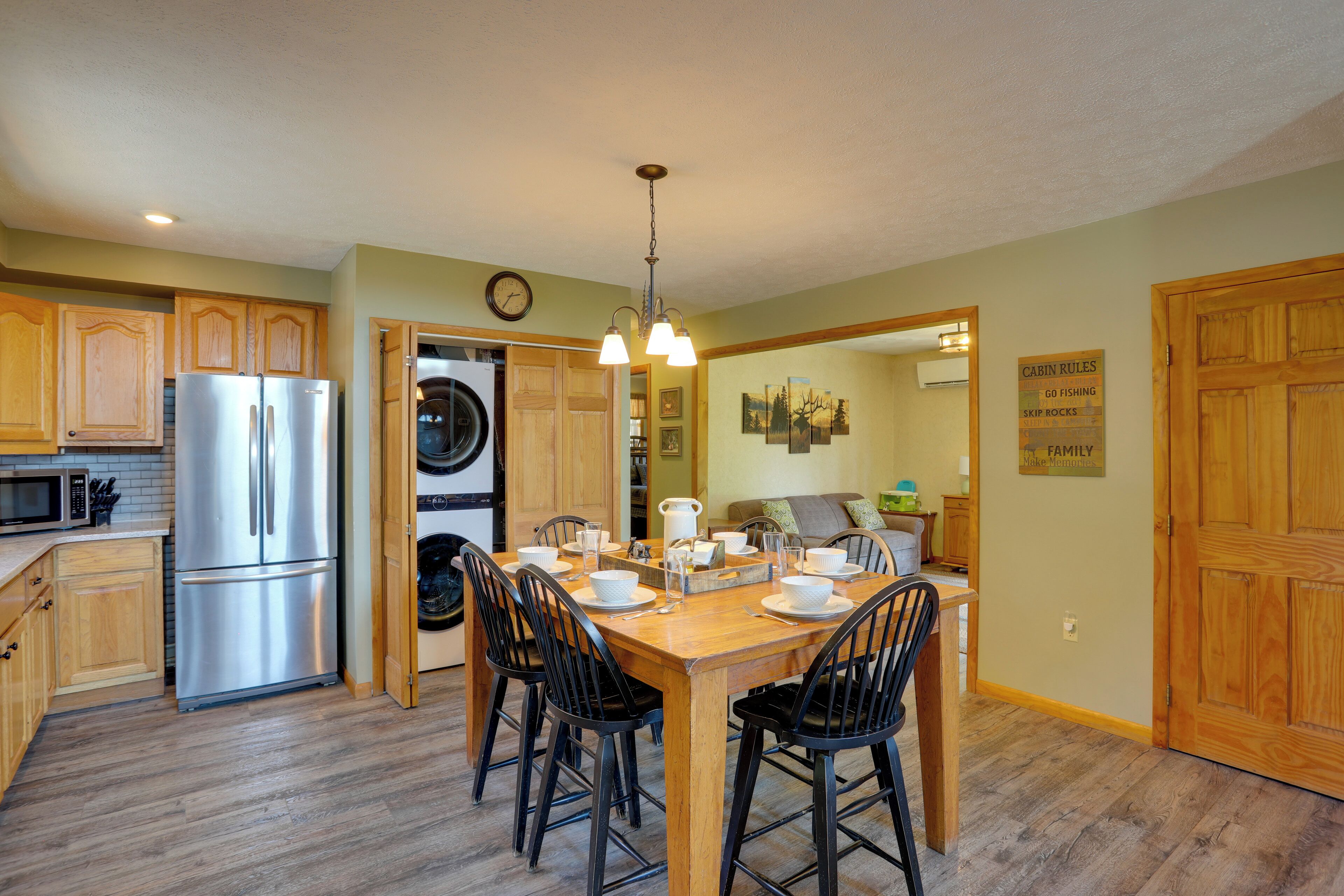 A kitchen with wooden cabinets, a stainless steel refrigerator, a washing machine, and a dining area with a wooden table and chairs.