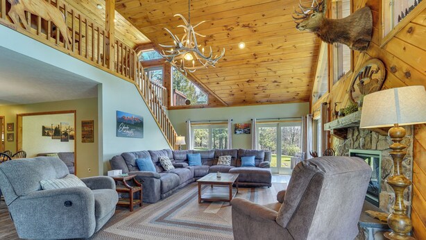 A spacious living area with a large sectional sofa, a fireplace, and a wooden ceiling with antlers mounted on the wall. - 3-acre Benezette Cabin: Hot Tub, Grill & Mtn View (Benezette)