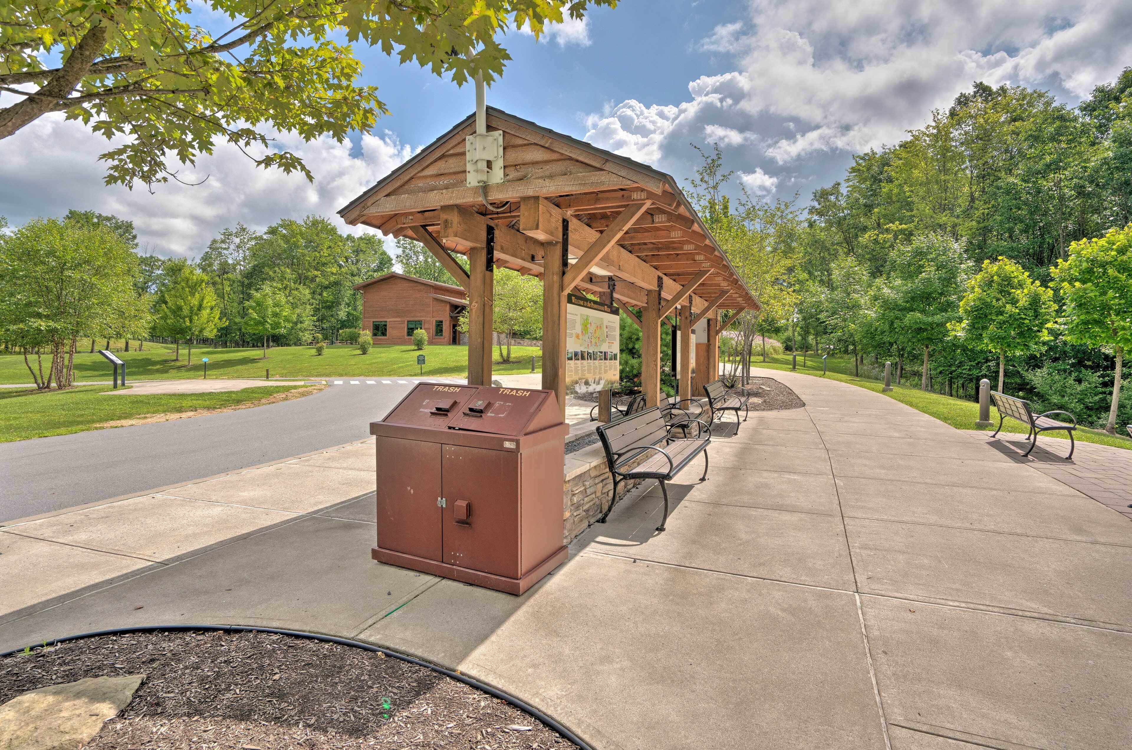 A covered pavilion with benches and a trash can in a park setting.