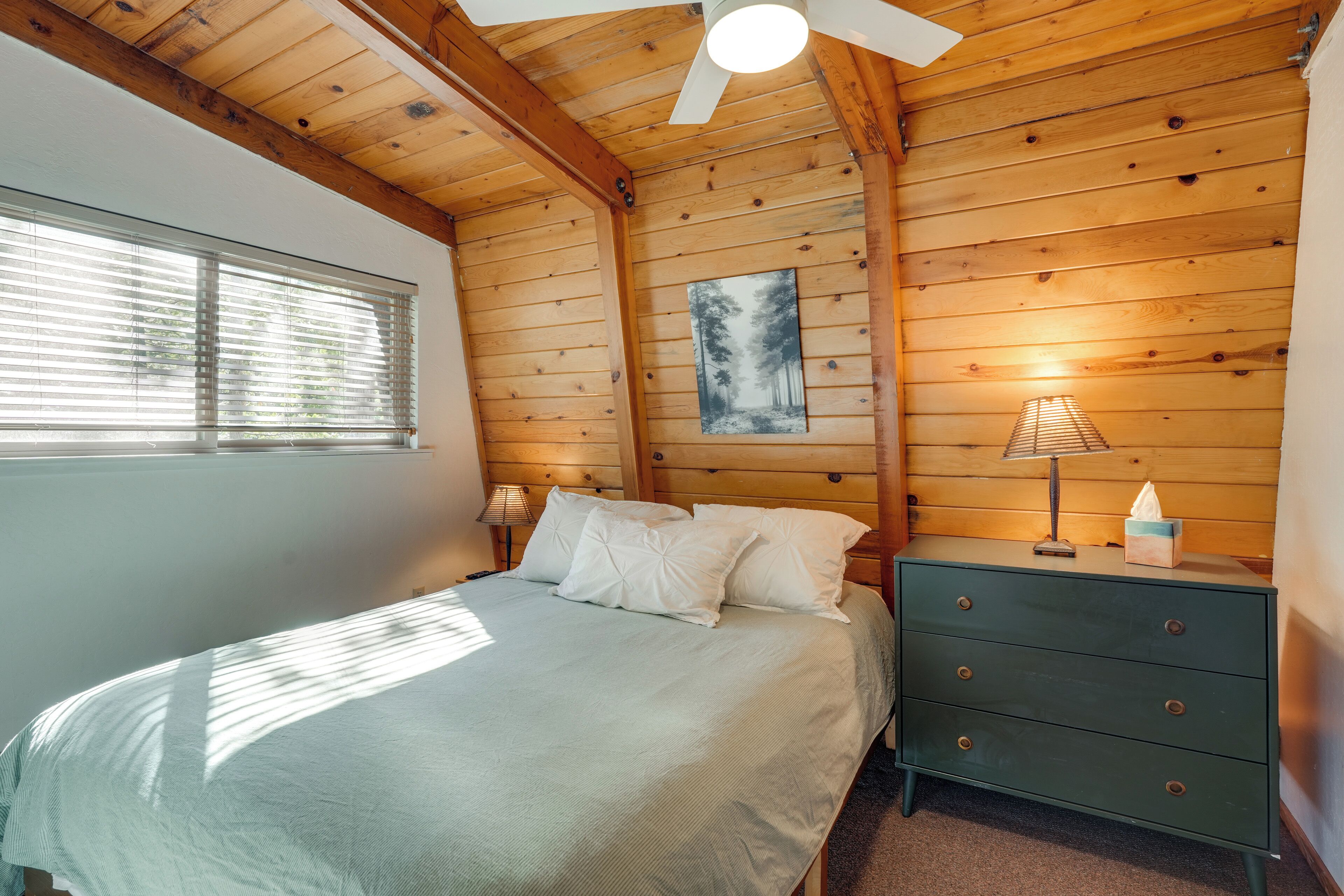 A bedroom with a bed, a nightstand, a dresser, a painting on the wall, and a ceiling fan.