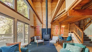 Un intérieur de chalet chaleureux avec une cheminée centrale, des poutres en bois et un coin repas.