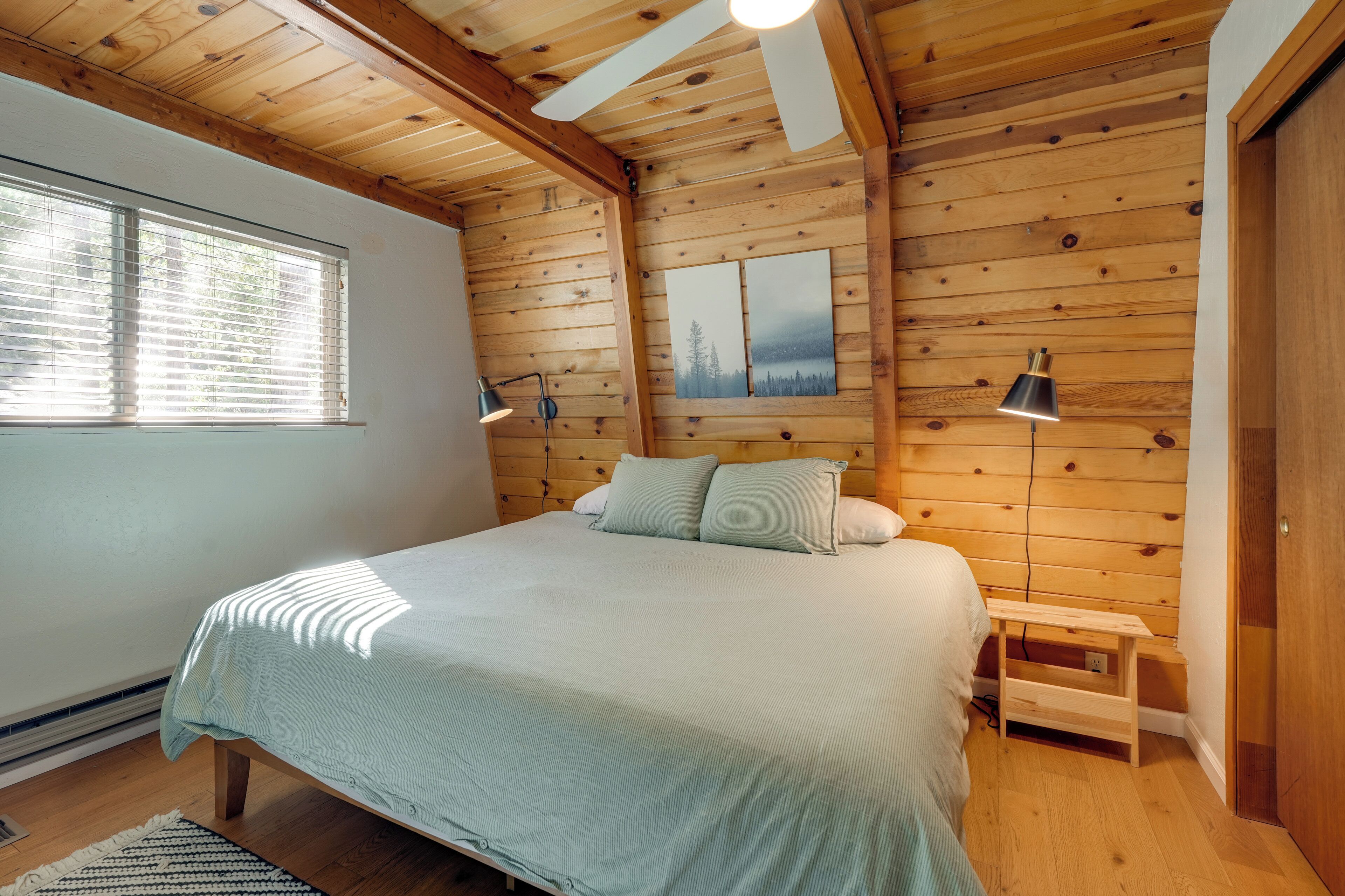 Een slaapkamer met een houten plafond, een bed met een lichtgekleurd beddegoed, twee bedlampen en een klein houten nachtkastje.