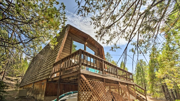 Une cabane dotée d’une terrasse en bois et d’une grande fenêtre, entourée d’arbres.