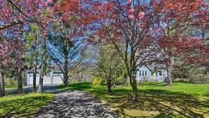 Un sentier pavé dans un parc, avec des arbres, une maison et un garage en arrière-plan.