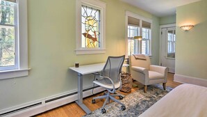 Une chambre comprenant un bureau, une chaise, un lit et une fenêtre ornée de vitraux.