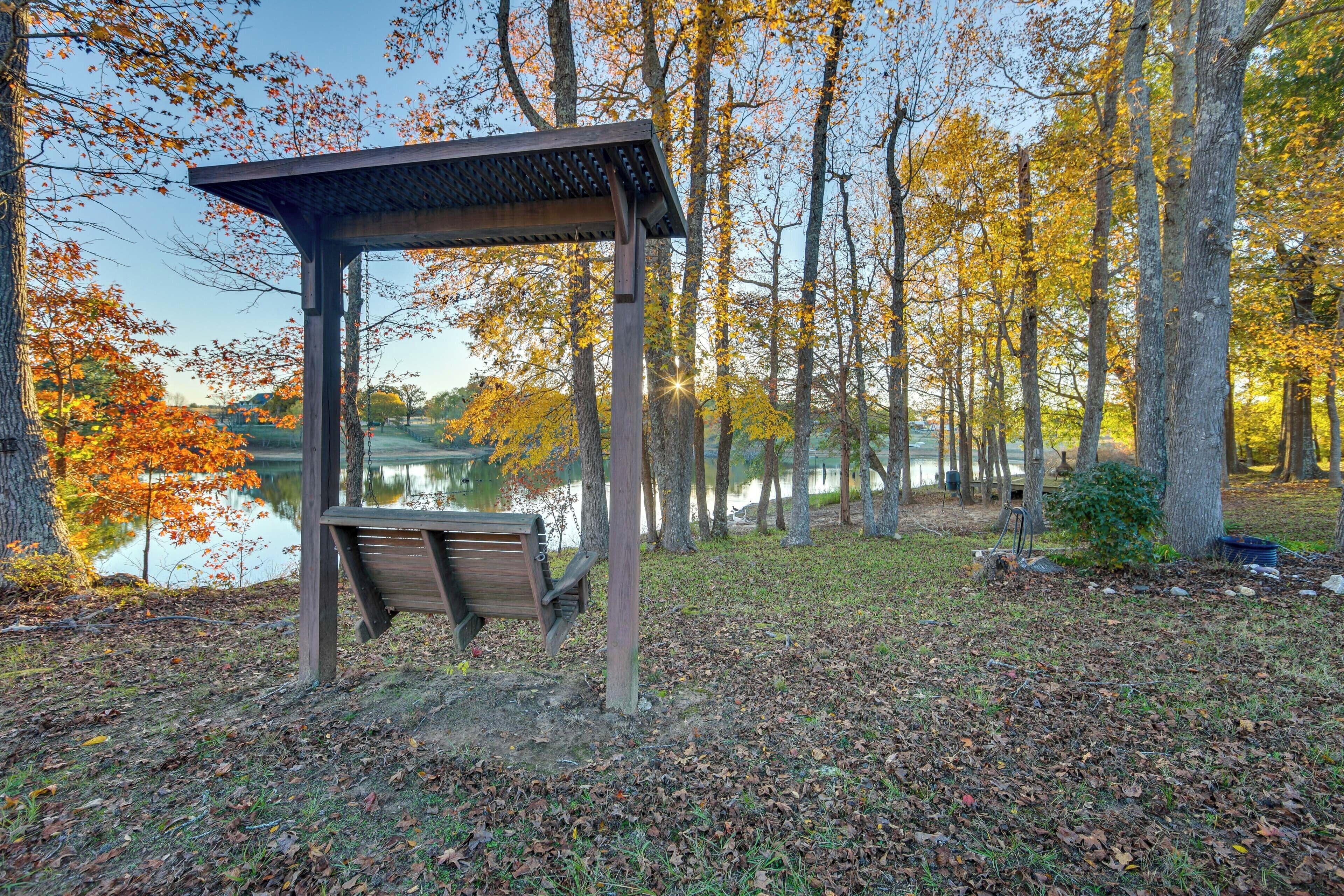 Un mirador de madera con un banco, rodeado de árboles y un lago.