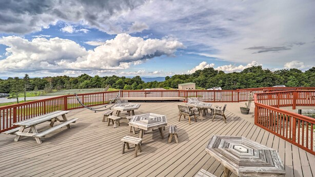 A wooden deck with picnic tables and benches, surrounded by a red railing, overlooking a forested area. - Resort Amenities: Beech Mtn Condo Near Skiing! (Banner Elk)