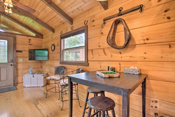 A wooden cabin interior with a dining table, two chairs, a television, and a small cabinet.