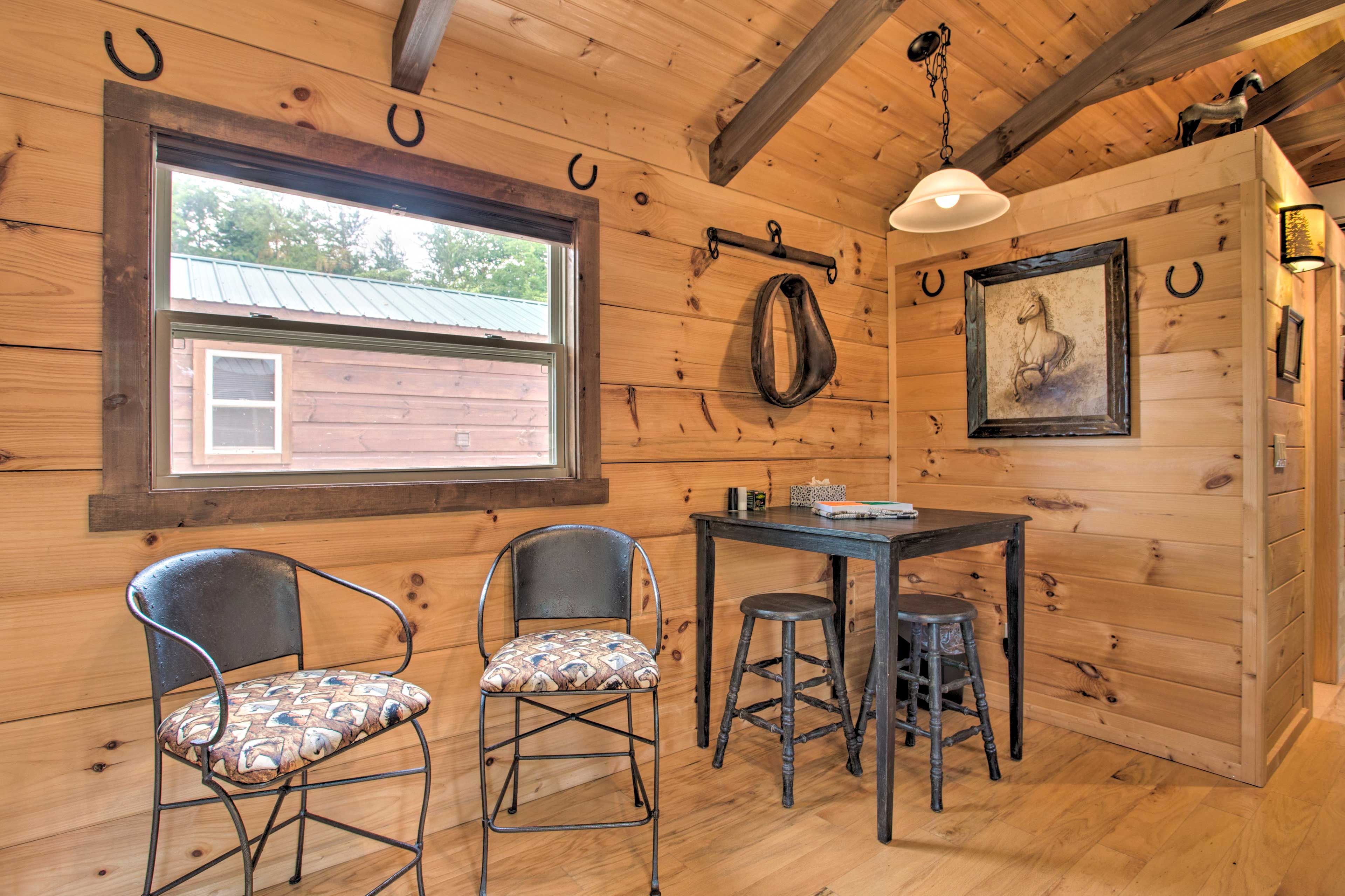 A wooden interior with a table and two chairs, a window, and a hanging light fixture.