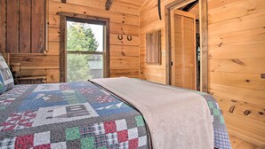 A wooden cabin bedroom with a quilted bedspread, wooden walls, and a window. - Near Winter Trails! Rustic Cabin in Mill Spring (Mill Spring)