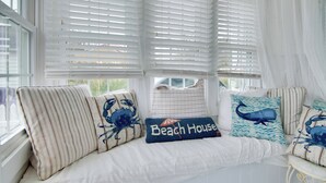 A bedroom with a large window, white blinds, and a bed with multiple pillows, including one with a beach house design. - 'chincoteague Charm' Escape w/ Bikes & Yard Games! (Chincoteague)