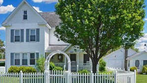 A two-story house with a front porch, a white picket fence, and a large tree in the yard. - 'chincoteague Charm' Escape w/ Bikes & Yard Games! (Chincoteague)