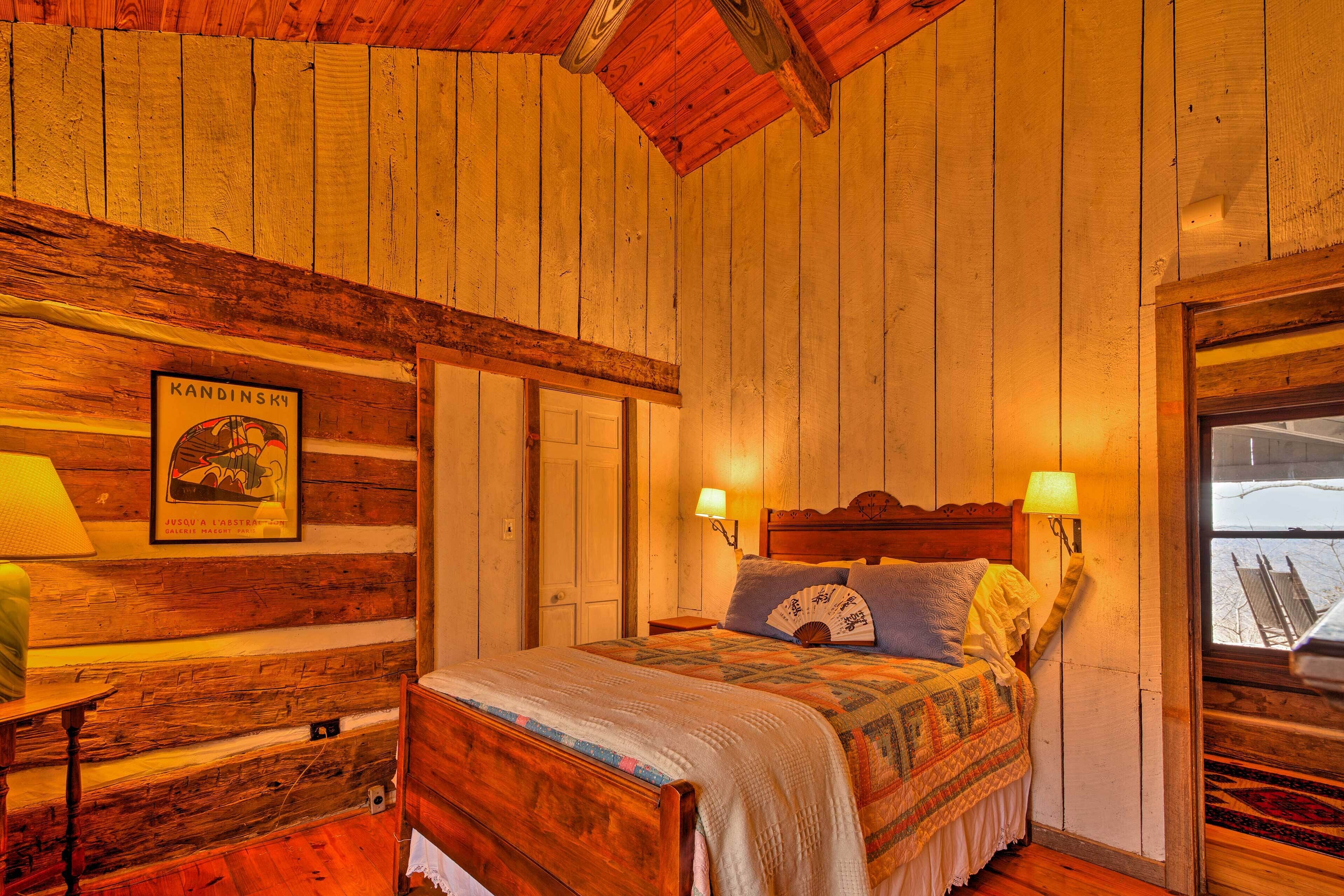 Habitación de cabaña de madera con cama, dos lámparas de noche, un cuadro en la pared y ventana con vista a un paisaje nevado.