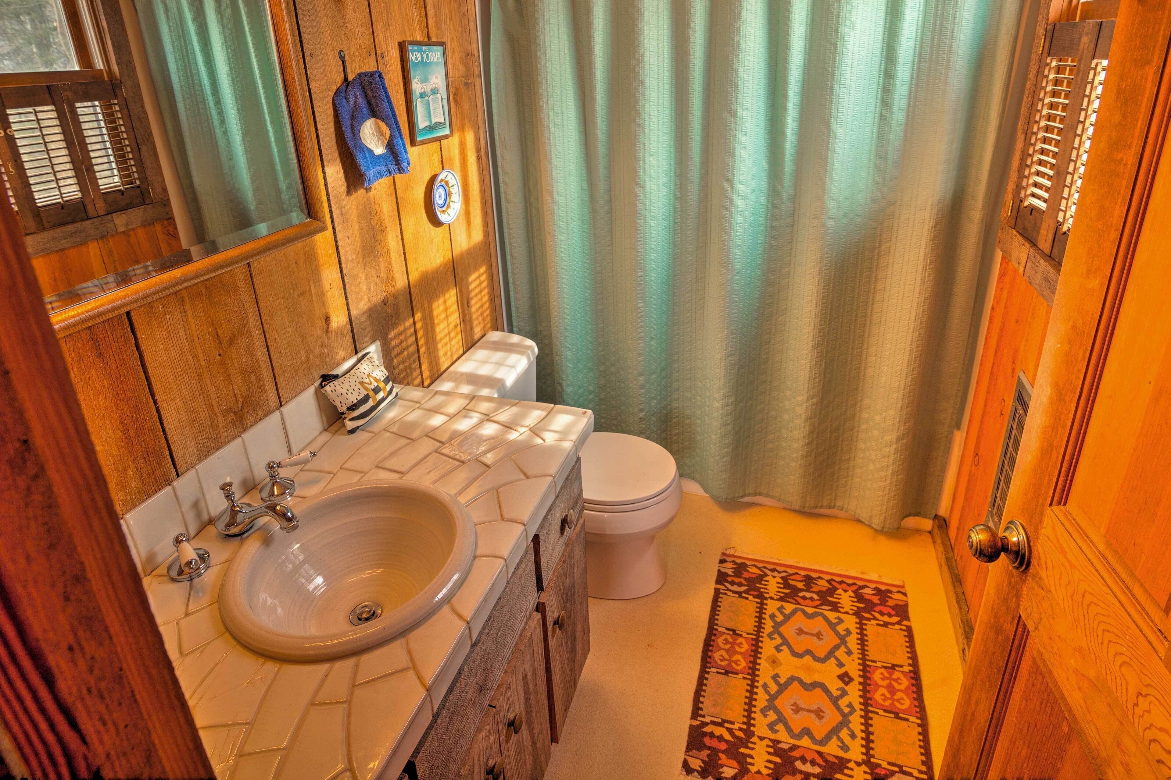 A bathroom with a wooden vanity, a sink, a toilet, and a patterned rug on the floor.
