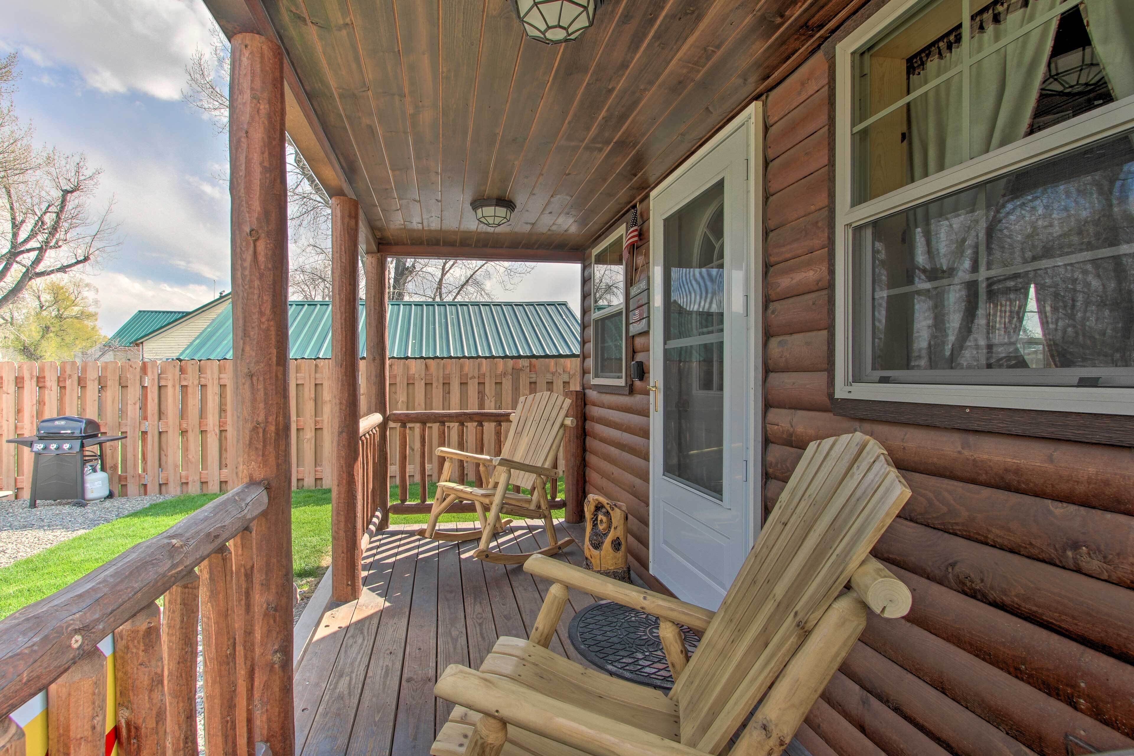 A wooden deck with two rocking chairs and a grill, a wooden door, and a window with curtains.