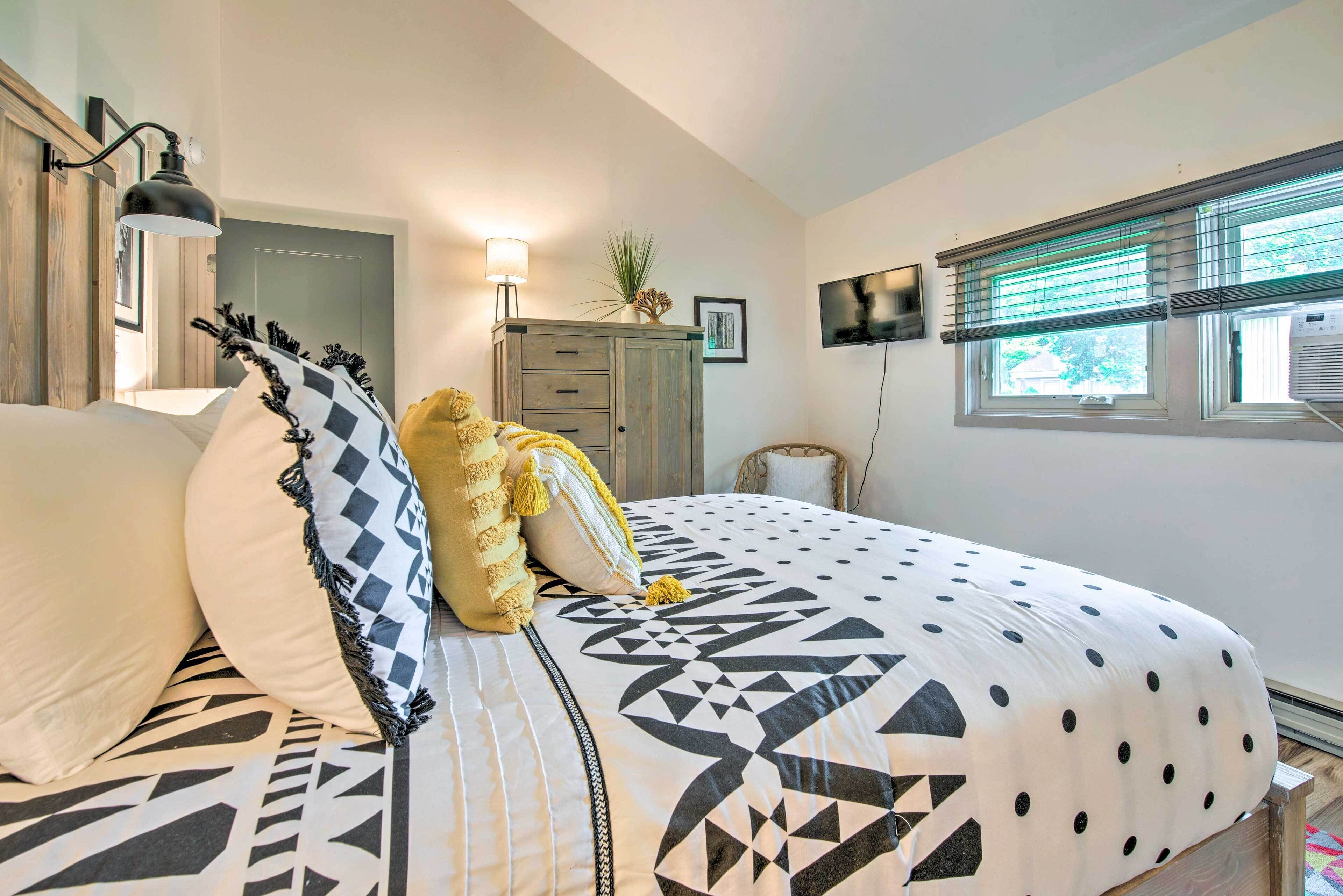 Une chambre à coucher avec un grand lit, une table de chevet, une lampe, une commode et une fenêtre avec des stores.