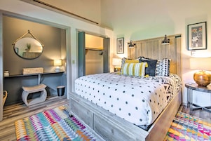 Un dormitorio con cama, espejo, armario, un pequeño taburete y una alfombra colorida.