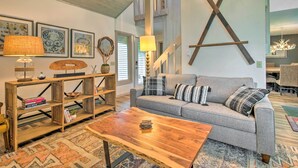 A modern living room with a grey sofa, wooden coffee table, and a bookshelf. There are framed artworks on the wall and a large wooden X on the wall. - Cortland Abode: 1 Mi to Greek Peak Mountain Resort (Cortland)