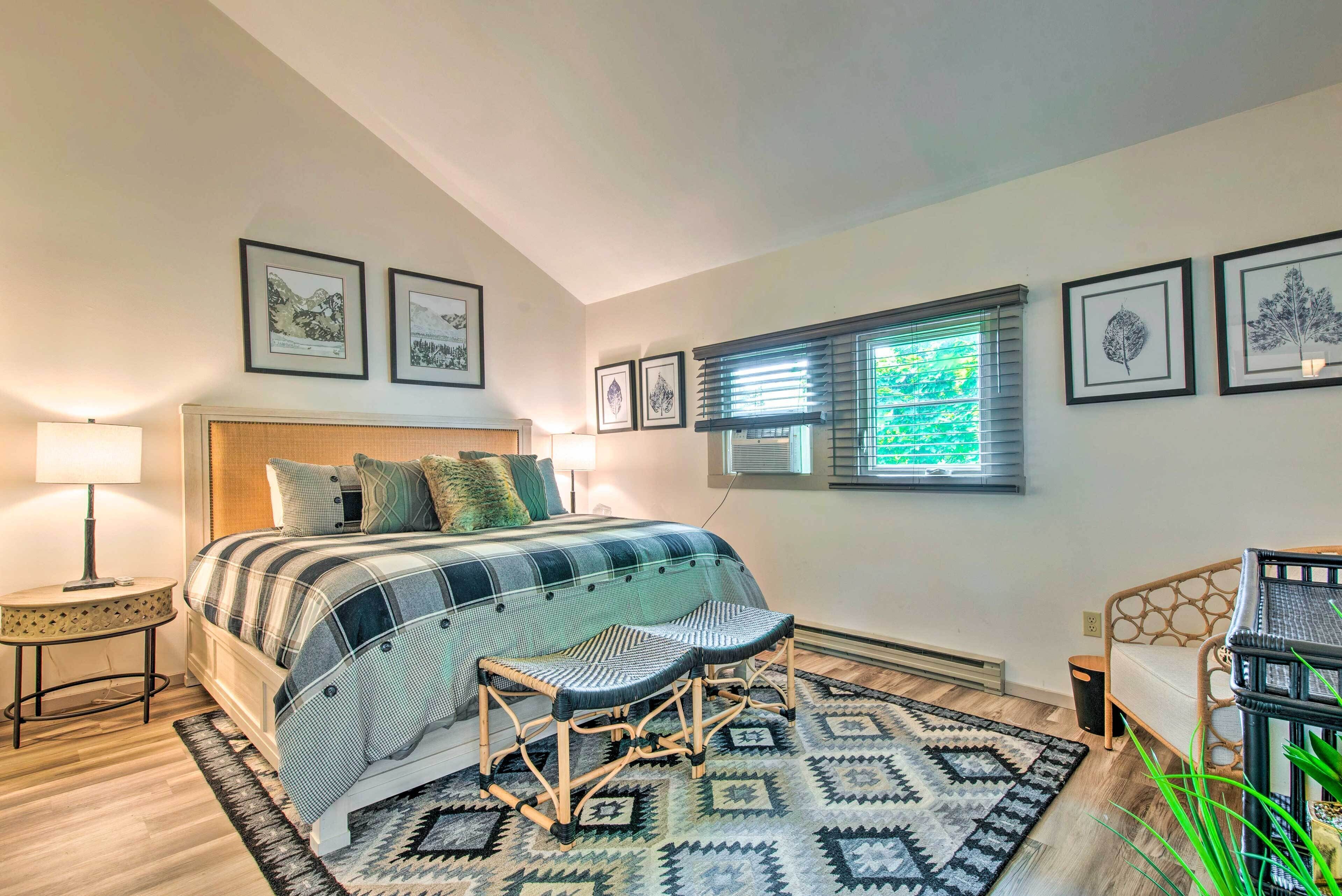 Une chambre à coucher avec un lit, deux chaises, une table de chevet, une lampe, une fenêtre avec des stores et des tableaux encadrés accrochés au mur.
