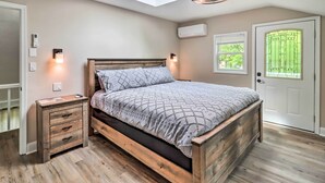 Une chambre avec un puits de lumière, un lit recouvert d’une couvre-lit à motifs, des lampes de chevet, une table de chevet en bois et une porte blanche avec une fenêtre.