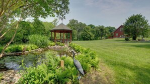 A gazebo, a pond, and a red house in a lush garden.