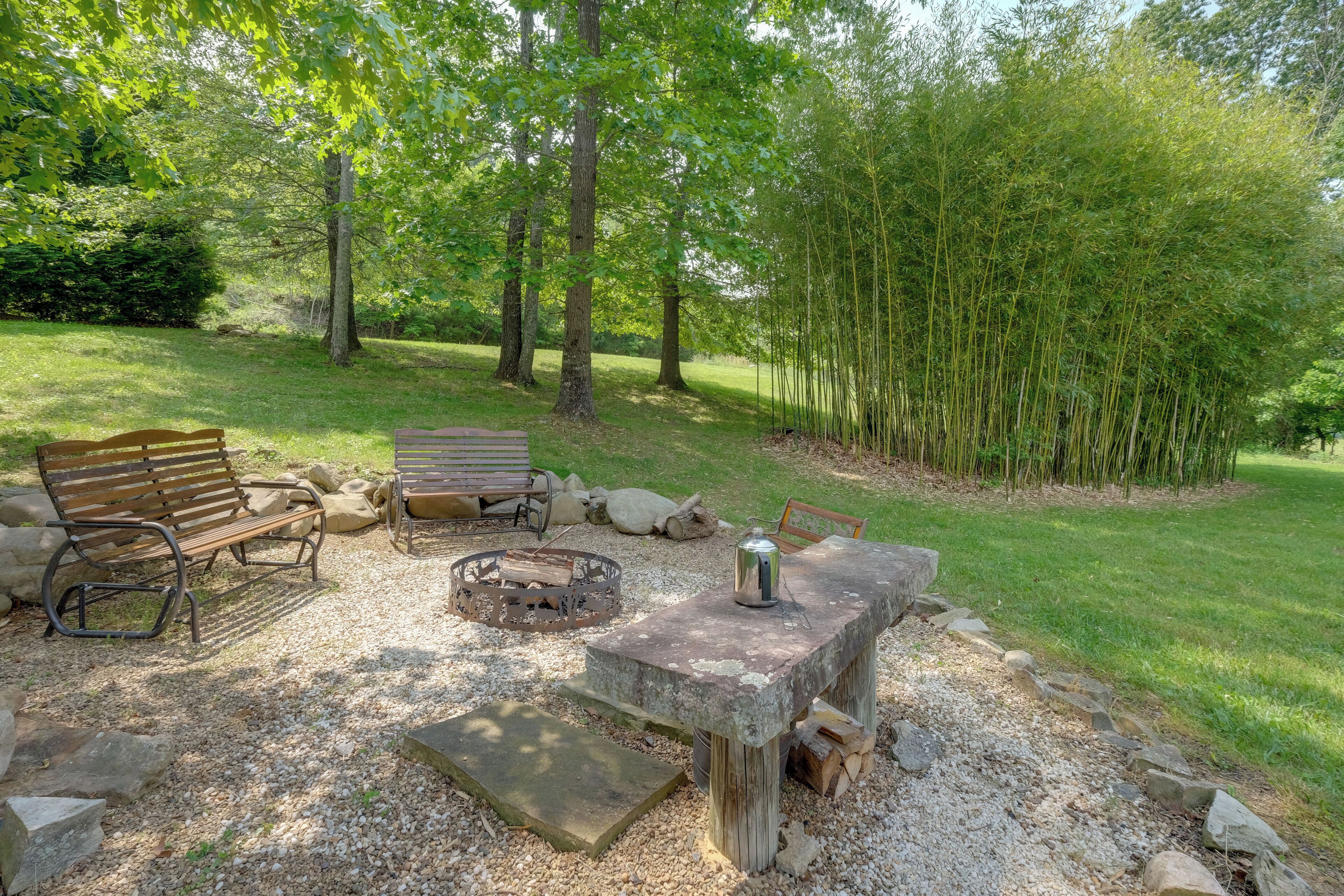 A rustic outdoor seating area with a stone table, two benches, and a fire pit.