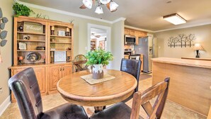 A dining area with a round wooden table, leather chairs, a ceiling fan, and a kitchen in the background.