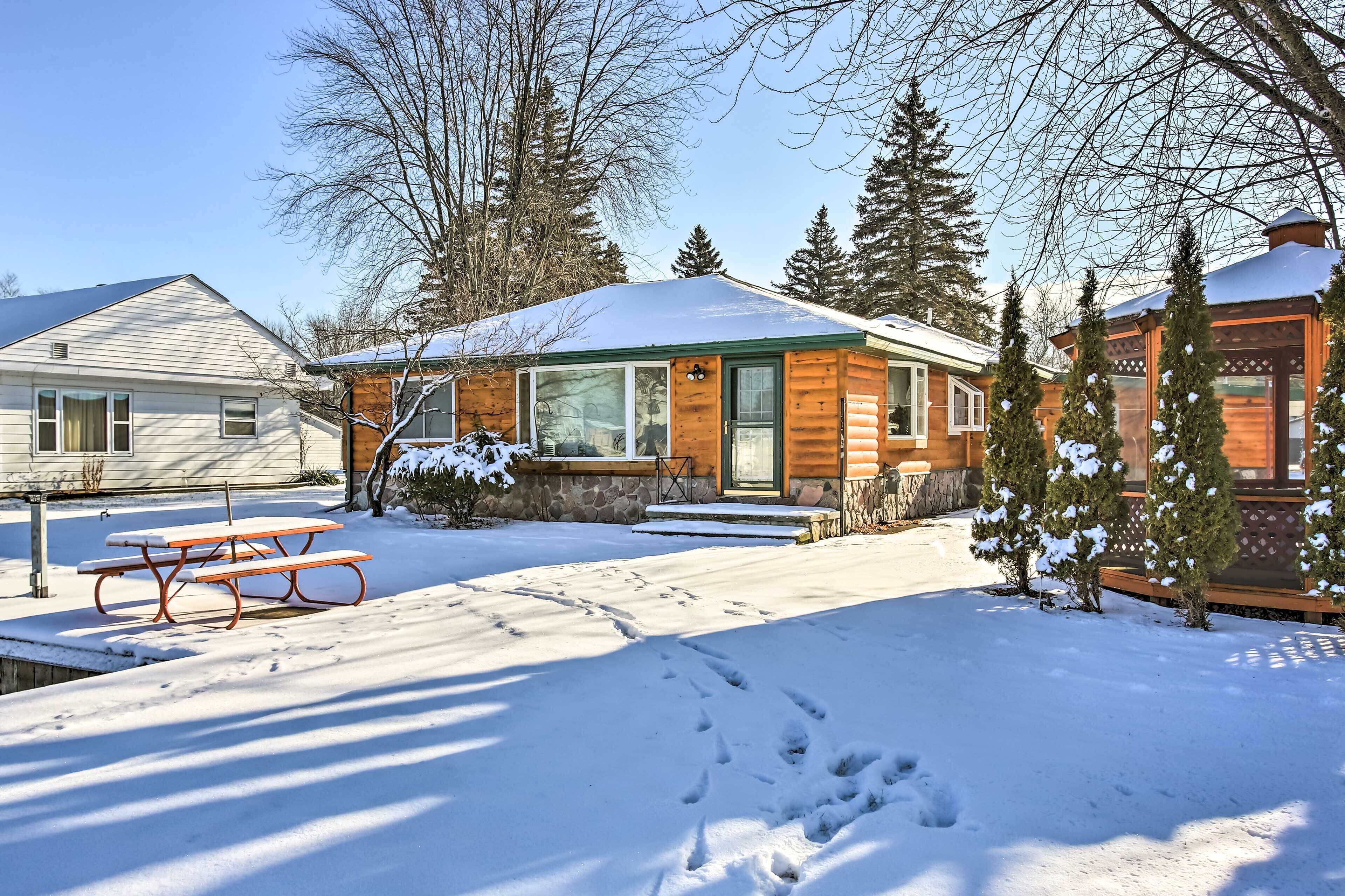 A wooden cabin with a snow-covered roof, a picnic table, and a stone pathway leading to the entrance.