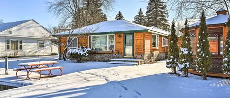 A wooden cabin with a snow-covered roof, a picnic table, and a stone pathway leading to the entrance.