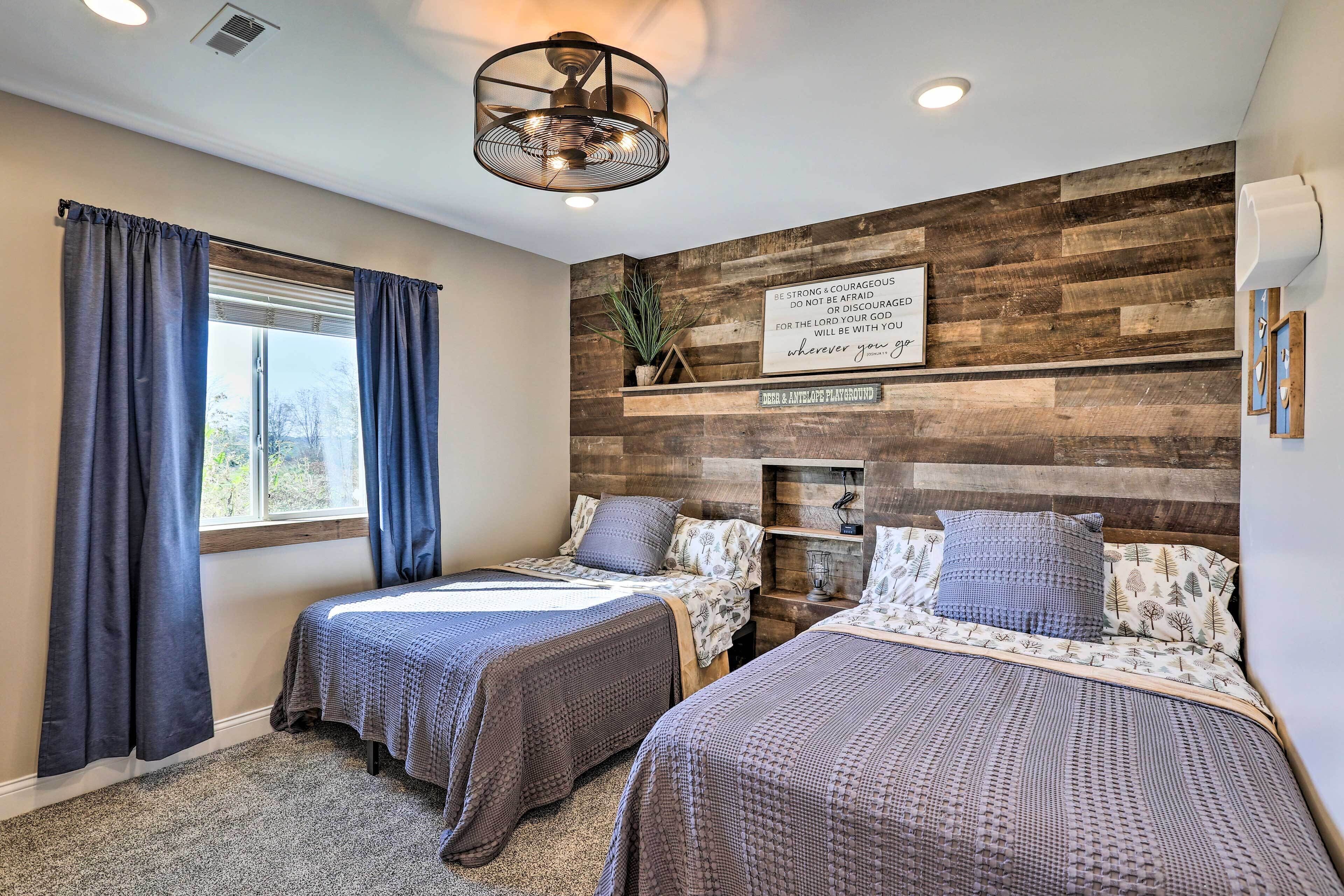 A bedroom with two beds, a wooden wall panel, a ceiling fan, and a motivational quote on the wall.